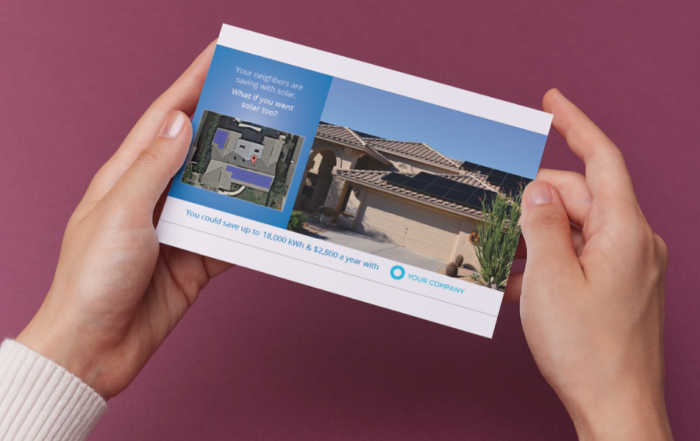 A person holding a postcard showing a house with solar panels and a message promoting solar energy savings.