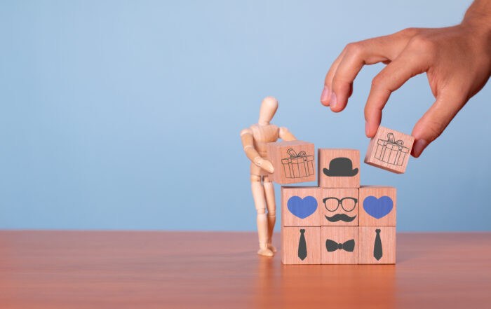 A wooden mannequin arranging blocks with images of gifts, hearts, and accessories, symbolizing personalization and thoughtful presentation.