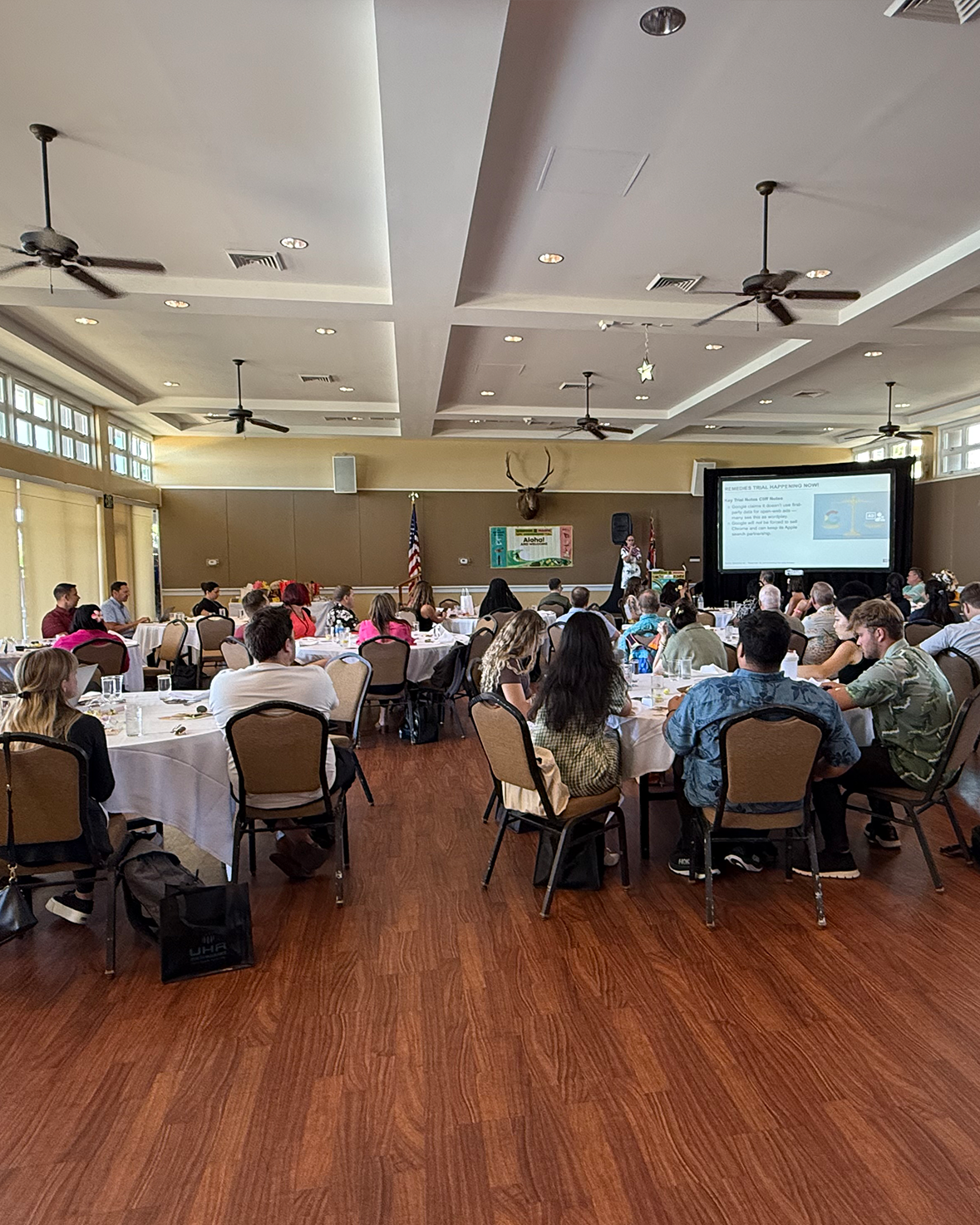 Anna Covert delivering a keynote presentation for AAF AdWest Hawaii to a seated audience in a conference room, speaking in front of a large screen with attendees gathered at round tables.